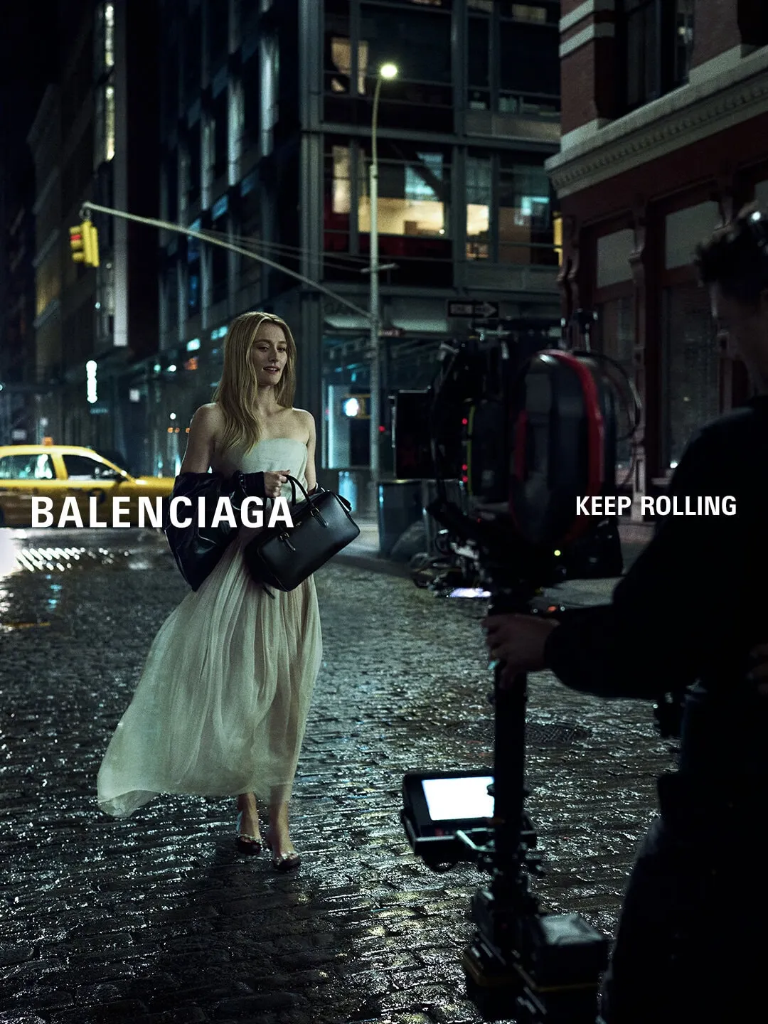 A Balenciaga campaign shoot on a rain-slicked New York street, with an actor in a pale dress facing a cinema camera and crew