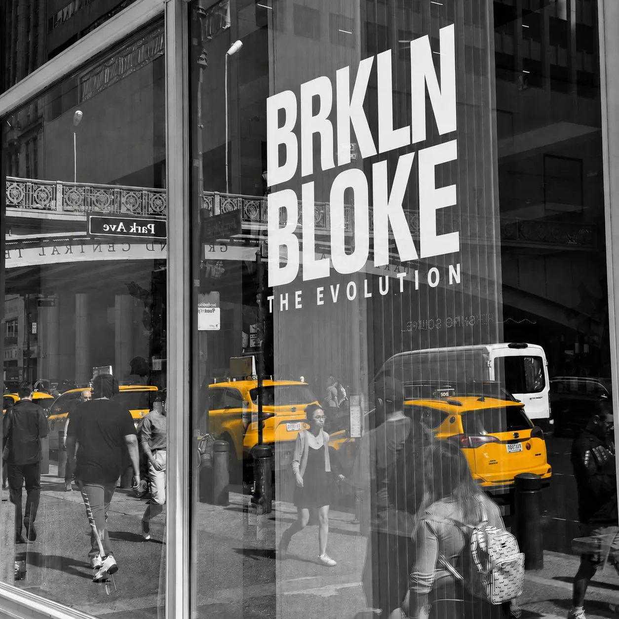 The BRKLN BLOKE window reflected against Grand Central, with yellow taxis in colour on the street