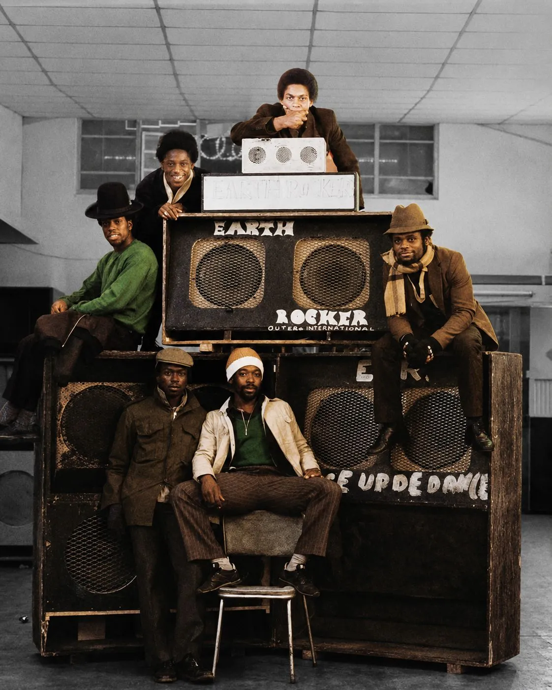 Six men gathered around the Earth Rocker sound system, their clothes in muted colour against a monochrome room