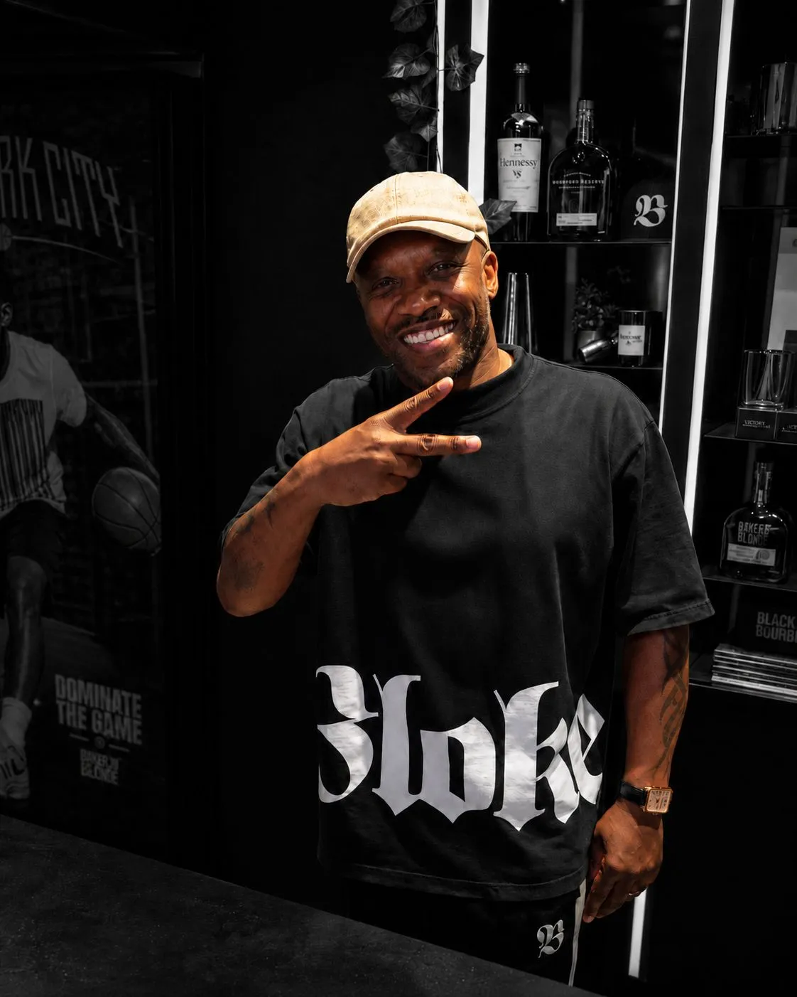A smiling man in a gold cap and black Bloke shirt, picked out in colour inside a monochrome store