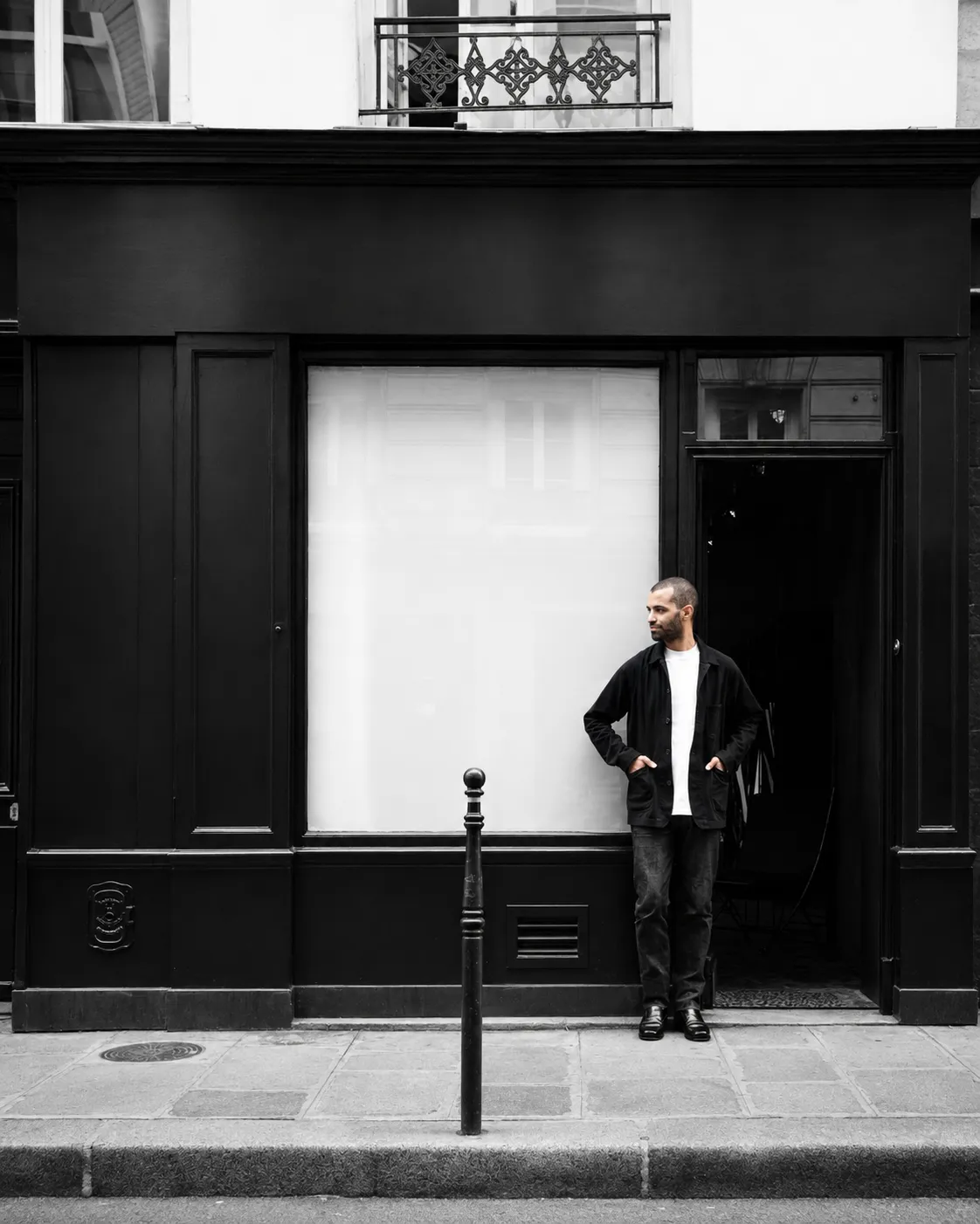 A man dressed in black standing beside the doorway of a monochrome Paris boutique with an unmarked black frontage