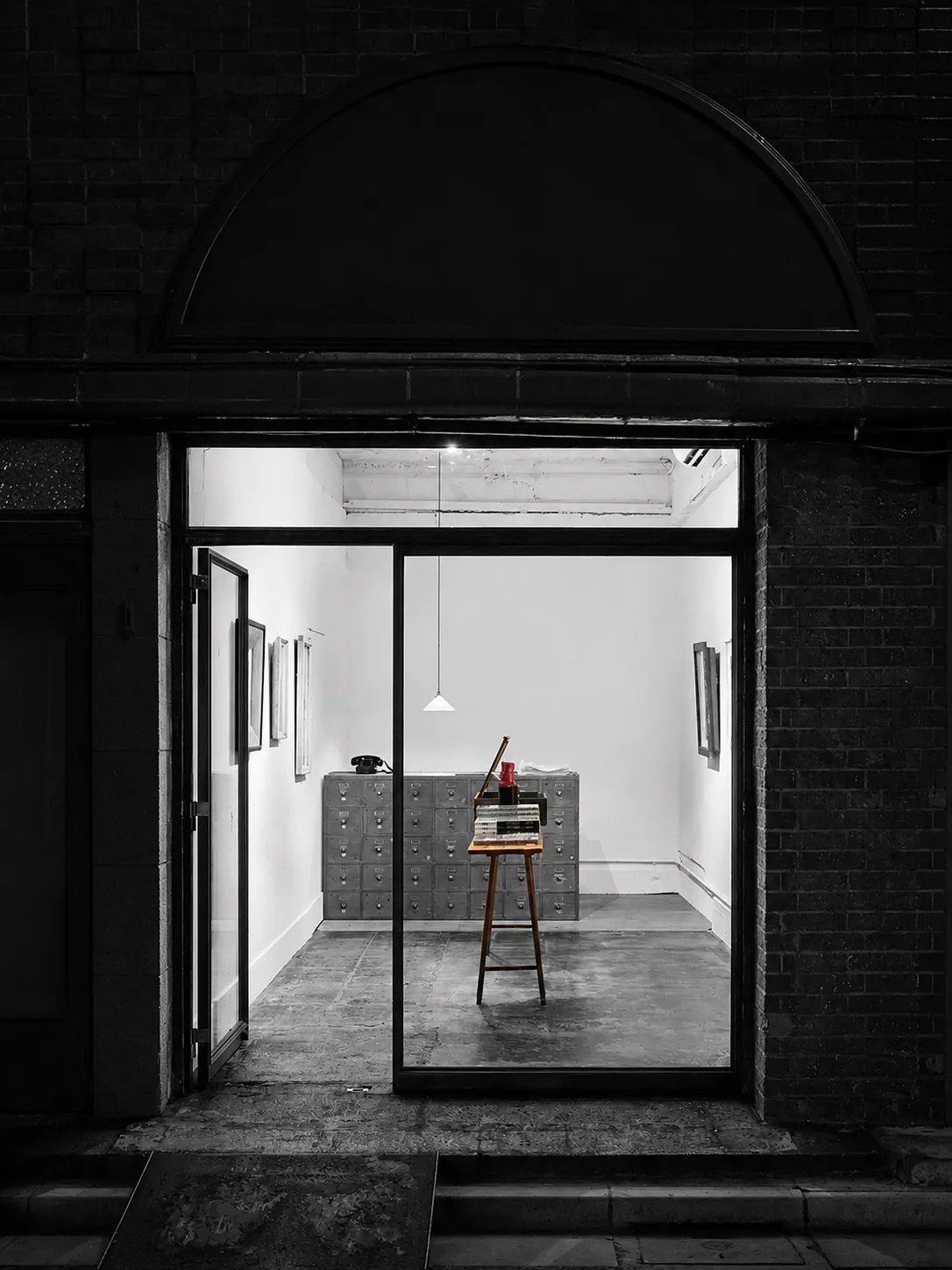 A single book displayed on an easel inside Morioka Shoten, its red binding the only colour in the dark storefront