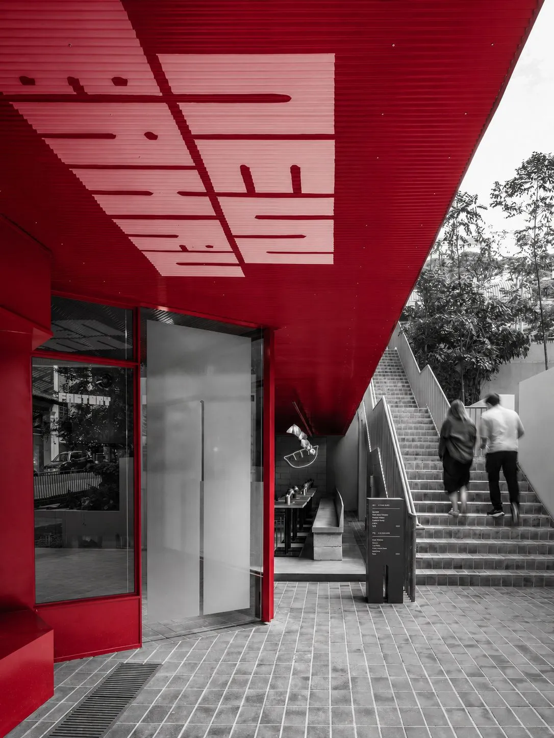 A red architectural canopy frames the entrance to New Bahru while two visitors climb the stairs