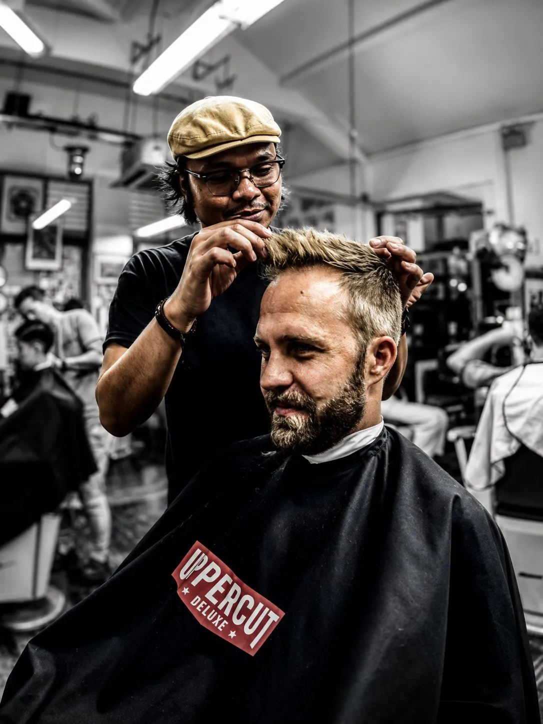 A barber shapes a customer’s hair inside The Panic Room, with a red clipper label in colour against the monochrome shop