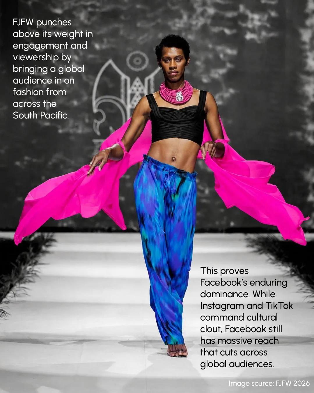 A model in a pink wrap and blue print trousers mid-stride on the runway