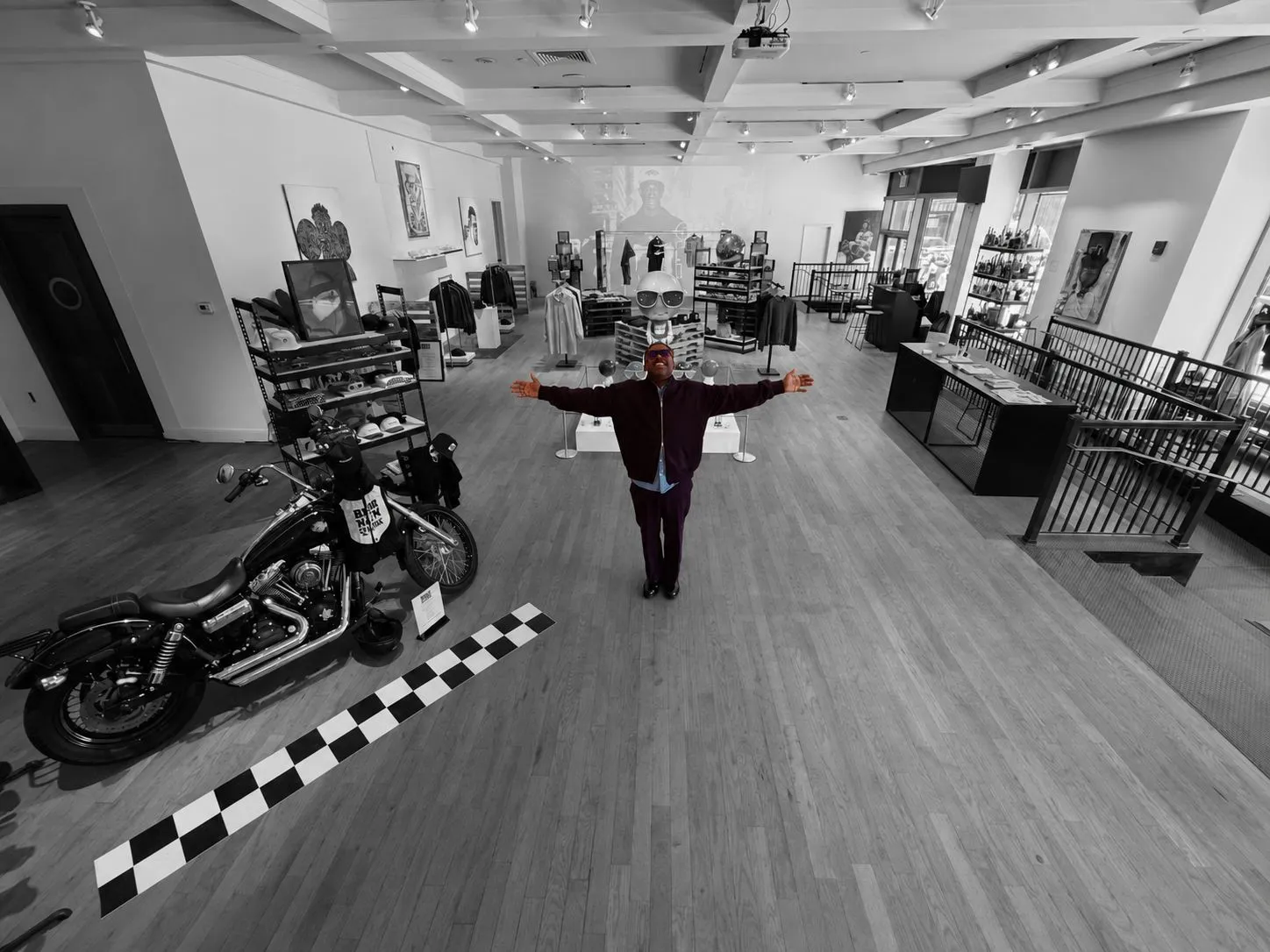 A man with his arms open at the centre of BRKLN BLOKE’s monochrome store, his clothes and sunglasses picked out in colour