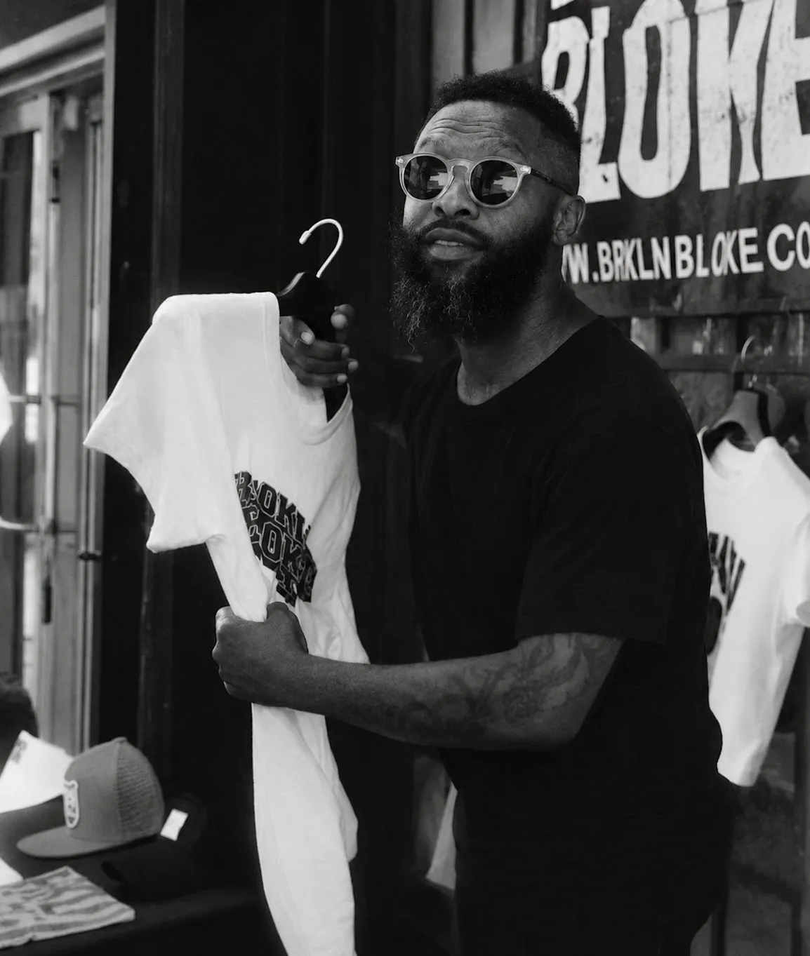 Wayne Fortune holding up a white BRKLN BLOKE T-shirt at a street-side table